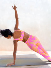 Modèle en legging rose et orange taille haute motif rétro en posture de yoga.
