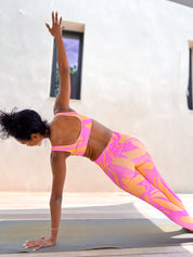 Modèle en legging rose et orange taille haute motif rétro en posture de yoga.